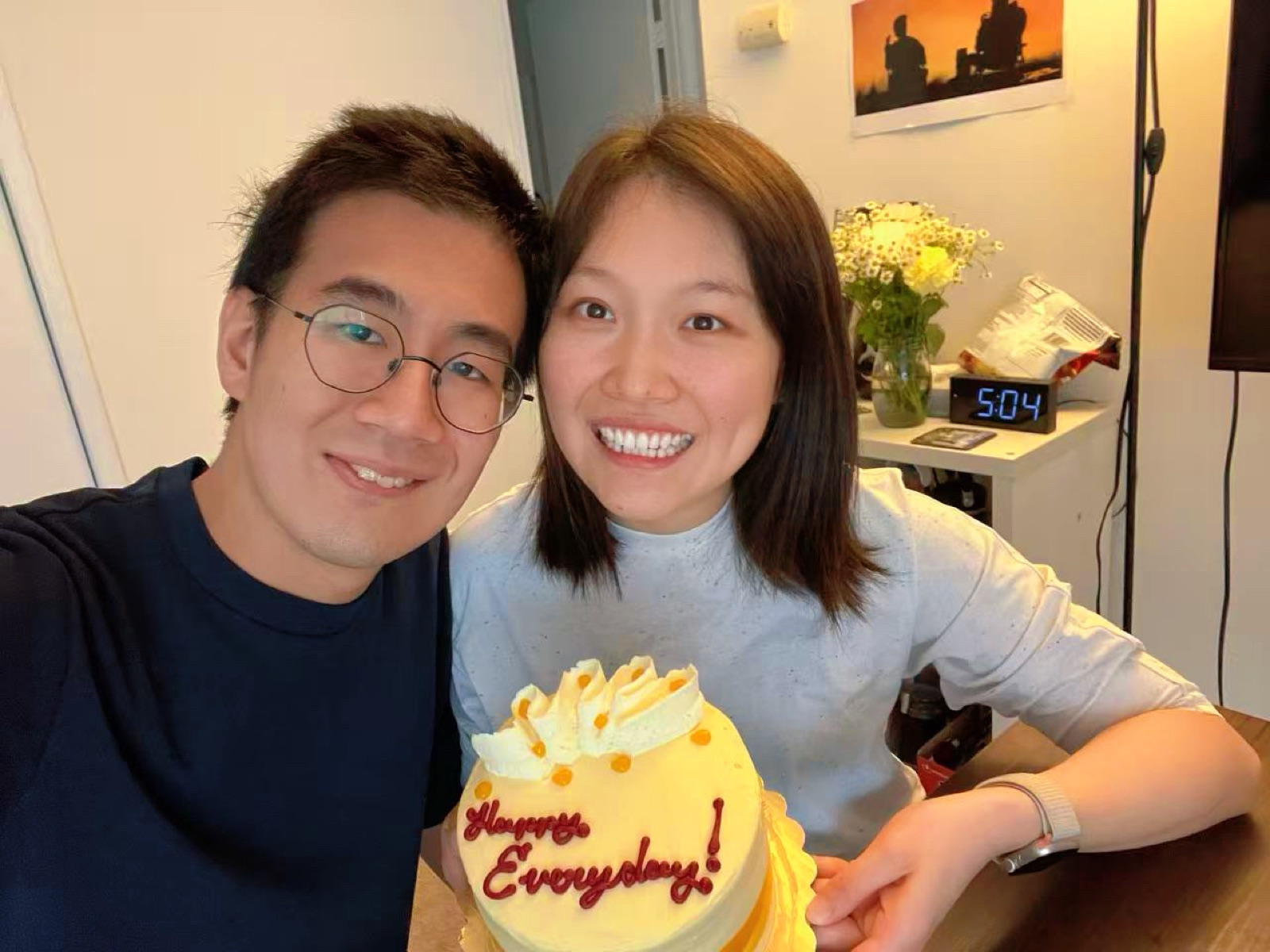 The couple smiling beside a small cake iced with the words Happy Everyday