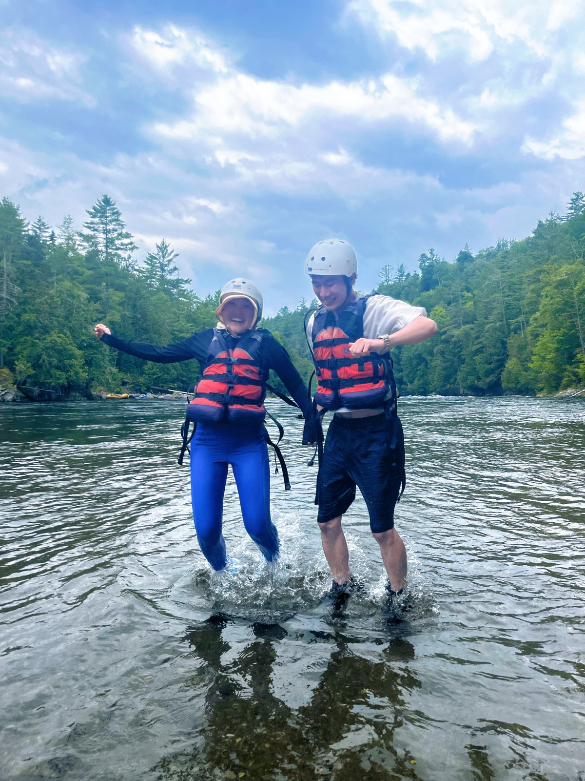 The couple jumping above a river in life jackets and helmets on a white-water rafting trip