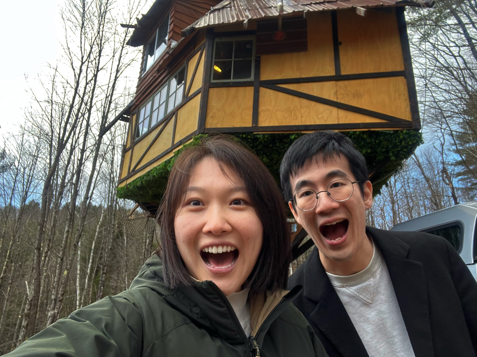 The couple smiling in front of a handcrafted treehouse in a winter forest
